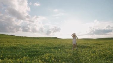 Kırsal kesim, beyaz elbiseli neşeli genç bir kadının arka planı kolza tohumu tarlasında koşuyor, 4k yavaş çekim..