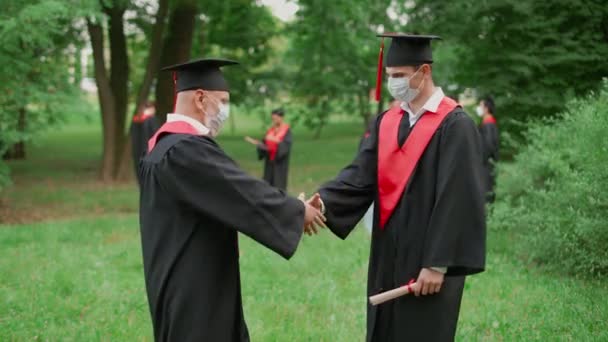 国际大学毕业典礼上 资深讲师祝贺男同学获得毕业文凭 老师和戴着口罩的学生握手 慢动作4K — 图库视频影像