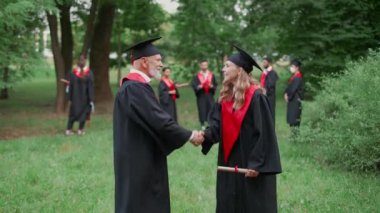 Uluslararası üniversite mezunu, kıdemli öğretim üyesi, diplomasını aldığı için mezun olan kadını tebrik ediyor. Mezuniyet cüppeli bir kadın, elinde bir diploma tutuyor. Duygusal bir an..