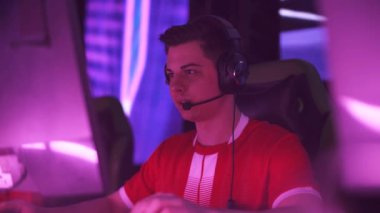 Kulaklık takan, video oyunu oynayan, siber sporcu şampiyonada takımla iletişim kuruyor, yoğun oyun, kırmızı neon ışığı..