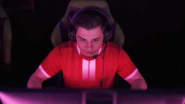 Kulaklıkla odaklanmış bir oyuncunun portresi, video oyunu oynuyor, siber sporcu şampiyonada takımla iletişim kuruyor, takım turu kazanıyor, kırmızı neon ışığı..