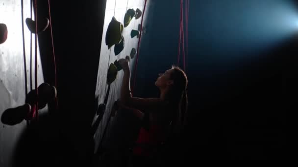 从侧面看 女攀登者在攀岩墙上接受训练 练习攀岩和爬山 用保险爬上悬崖 用电影照明 — 图库视频影像