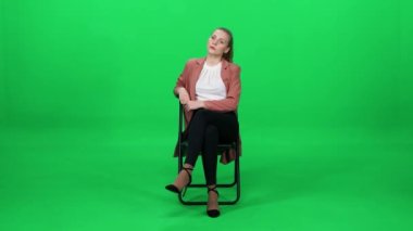 Ofis sandalyesinde oturan beyaz bir kadın, yeşil arka plan, zarif bir kadın, bekleme süreci..