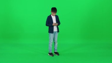 Yeşil arka planda duran ve bir cep telefonuyla konuşan, krom anahtar üzerinde şablon çizen takım elbiseli Asyalı çocuk..