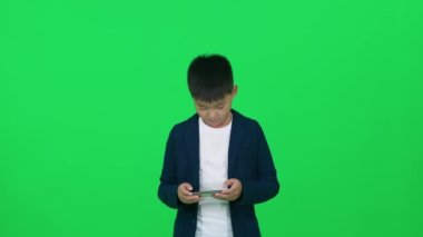 Gezici oyun, takım elbiseli Asyalı okul çocuğu yeşil arka planda duruyor ve akıllı telefonda oyun oynuyor, kromatonda şablon çiziyor..