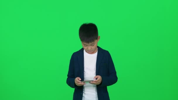 手机游戏 身穿西装的亚洲学生站在绿色背景上 用智能手机玩游戏 铬钥匙上的模板 — 图库视频影像