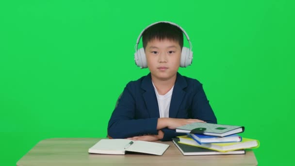 遠隔学習 リビングルームの机に座って自宅で勉強する無線ヘッドフォンのアジアの学校ボーイ ビデオ通話でオンラインホームスクーリング ノートブックで書きます 染色体 — ストック動画