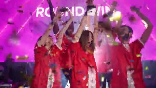 セレブレーション 勝利の感情 Eスポーツ選手の赤いチームは 国際選手権での勝利に喜び 女性は彼女の手に金杯を保持しています Confettiは空中で飛んでいる — ストック動画