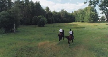 Erkek kovboyun ve bir kadının ormanın yakınındaki bir açıklıkta ata binişlerinin arka görüntüsü..