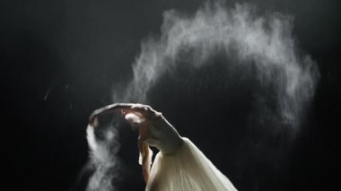 Dramatik dans, beyaz etekli zarif balerin, siyah arka planda dans edip koreografik öğeler sergilemek, magnezya kullanmak, karanlık sahnede sis etkisi, yavaş çekim..