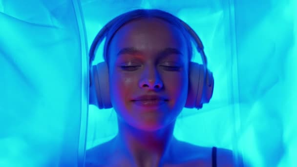 快乐的女人带着耳机躺在感觉剥夺室 霓虹灯 放松在温泉里 — 图库视频影像