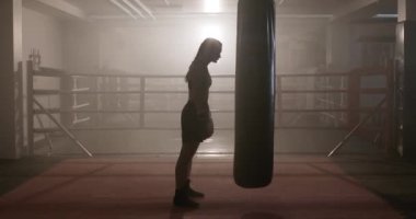 Boks, sıkı bir antrenmandan sonra kadın boksör, boks salonunda antrenman günü, yorgun kız kum torbasına düşer, arka ışıklandırma....
