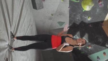 Dikey video, bir kadın tırmanıcının portresi tırmanma duvarının arka planına dayanır ve tırmanmadan önce magnezya kullanır.