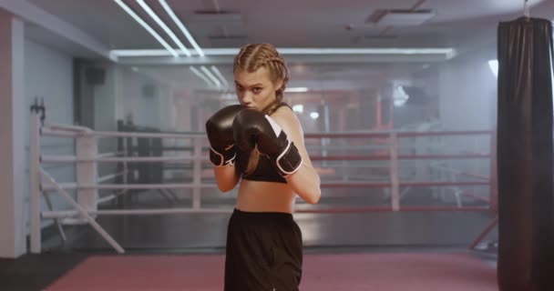 女性プロの戦闘機は彼のパンチを訓練し ボクシングジムでトレーニング 女性戦闘機は戦闘スタンスを取るとカメラを見て — ストック動画
