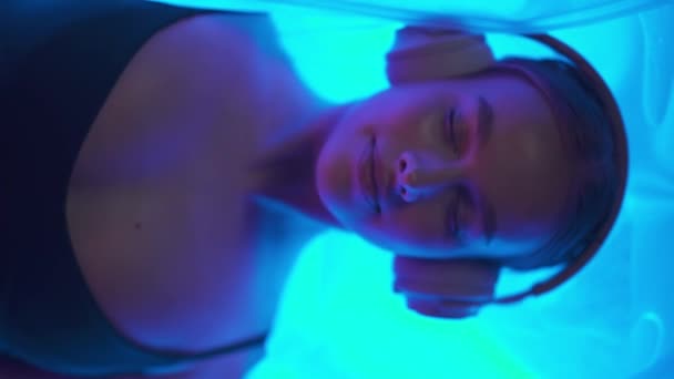 Handheld Vrolijke Vrouw Met Hoofdtelefoon Ligt Zintuiglijke Ontberingskamer Blauw Neon — Stockvideo