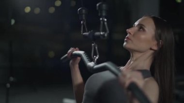 Spor salonundaki genç kadın blok blokları kaldırıyor, gece spor aletlerinde güç eğitimi alıyor..