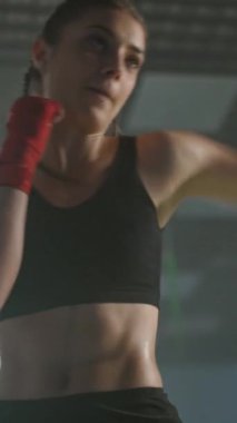 Beyaz kadın dövüşçü boks salonunda yumruklarını ve savunmalarını eğitiyor. Kız hızlı ve yavaş çekimde dikey video çekiyor..