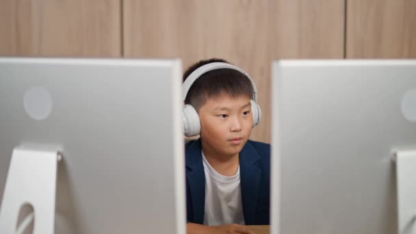 自宅で机に座っている間 アジアの少年を集中させ 10代の少年がモニターの背後でオンラインで働き 研究している — ストック動画