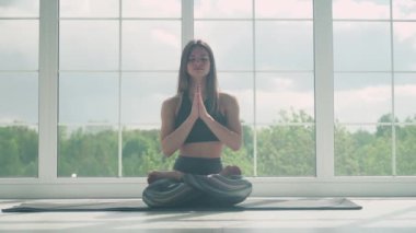 Sakinlik, genç bir kadın meditasyon yapıyor ve yoga yapıyor, sakin bir ruh hali, ışıkla dolu beyaz bir odada dinleniyor, yerde oturuyor, kamera hareket ediyor..
