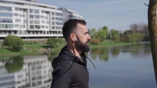 Dorosły Mężczyzna Biegnie Parku Niedaleko Miasta Podąża Kamerą Biegnie Słuchawkach — Wideo stockowe