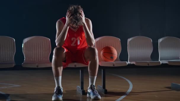 篮球比赛 一个从篮球比赛中恢复的疲惫的篮球运动员 过度劳累的坐在长椅上 — 图库视频影像
