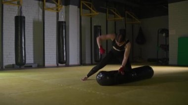 Sportif kadın boksör yumruklarını eğitiyor, yerde yatarken kum torbasına vuruyor, boks salonunda antrenman günü, formda vücut, yavaş çekim..