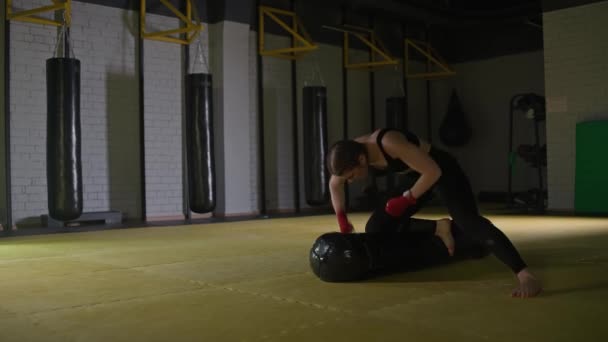 女性の戦闘機は彼のパンチを訓練します 床に横たわっている間パンチングバッグを打ちます ボクシングジムでのトレーニング日 強さフィットボディ 4Kスローモーション — ストック動画