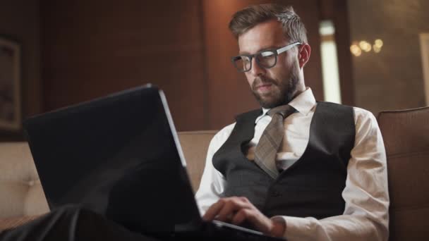 Молодой Бизнесмен Очках Работающий Ноутбуком Мужчина Костюме Сидящий Диване Отеле — стоковое видео