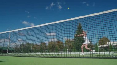 Yaz mevsimi, profesyonel tenisçi topa raketle vurur, tenis kortunda antrenman yapar, kadın topa vurur, top ağda kaybolur..