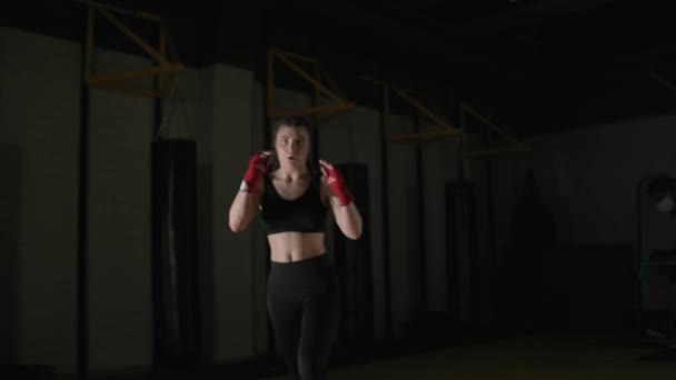 女性戦闘機は ボクシングジムで彼のキックを訓練します 若い女性は一連のパンチを訓練 フロントビュー 4Kスローモーション — ストック動画