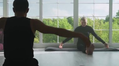 Sağlık, eklem yoga dersleri, bir erkek yetişkin bir kadına yoga öğretiyor, farklı yaşlardaki insanlar yoga yapıyor, ışıkla dolu beyaz bir odada dinleniyor, sakinlik....