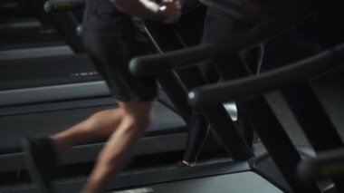 Gece eğitimi, koşu bandında koşan anonim bir koşucu, spor salonunda kadın antrenörle aerobik ve dayanıklılık eğitimi, bacak manzarası..