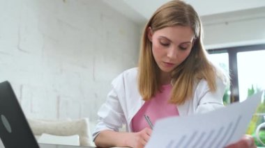 Odaklanmış kadın masasında oturup dizüstü bilgisayar kullanıyor, izolasyon sırasında çok çalışan bir yönetici, belgelerle çalışıyor ve raporlarla uğraşıyor..