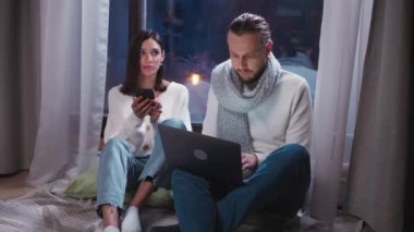 Kış zamanı, serbest çalışan biri yerde oturup dizüstü bilgisayarla çalışıyor, kız arkadaşı yanında oturuyor ve gece vakti akıllı bir telefon kullanıyor..