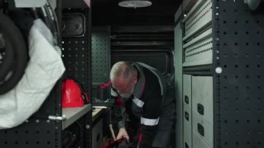 Saha çalışması, takım elbiseli gri saçlı işçi, teknik mühendis araçları bir minibüs deposundaki plastik bir alet kutusuna götürüyor, ekipman onarımı ve bakım hizmeti, işten önce hazırlık.