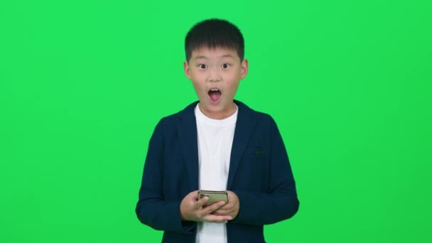 モバイルゲーム 緑の背景に立って スマートフォンでゲームをプレイするスーツのアジアのボーイ 少年はゲームに勝つことに喜び 染色体のテンプレート — ストック動画