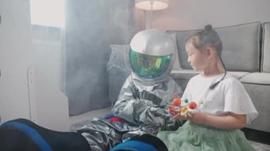 Asyalı çocuklar evdeki oturma odasında oynuyorlar, astronot kostümlü bir çocuk kız kardeşiyle yerde oturuyor, çocuklar güneş sisteminin oyuncak modeliyle oynuyorlar, yavaş çekim..