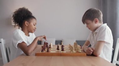 Evdeki çocuklar, esmer tenli bir kız ve beyaz bir oğlan oturma odasında oturmuş satranç oynuyorlar, eğlence, düşünce süreci..