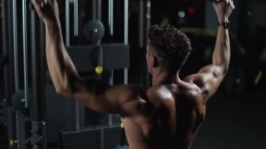 Gece vakti, spor salonundaki atletik adam jimnastik makinesindeki blokları kaldırıyor, blok aleti ve spor aletleri eğitimi alıyor, sinematik ışık..