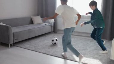 Yavaş çekim, kendini izole eden çocuklar, erkek ve esmer tenli kız oturma odasında futbol topuyla oynuyorlar, evde eğlence, iyi ruh hali..