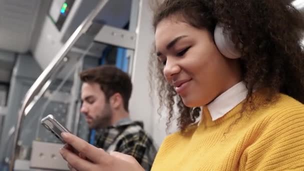 学生们乘坐地铁 用耳机听音乐 使用智能手机 在网上冲浪 乘坐公共交通工具 皮肤黝黑的女人 — 图库视频影像