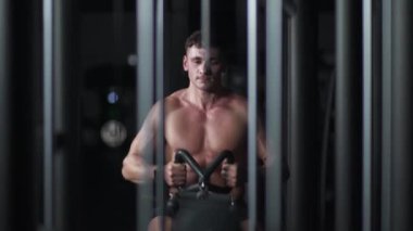 Spor salonundaki atletik adam kürek çekme makinesindeki blokları kaldırıyor, blok aleti ve spor aletleri eğitimi alıyor, gece vakti..