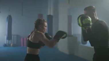 Kadın boksör yumrukları ve savunmayı eğitir, odaklanma eldivenleriyle kavga eder, boks salonunda koçla antrenman yapar, motivasyon sağlar..