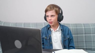Uzaktan öğrenme videosu, oturma odasında iş yerinde oturan ve kulaklıklı çocuk, evde kendini izole etmek için web kamerası kullanıyor..