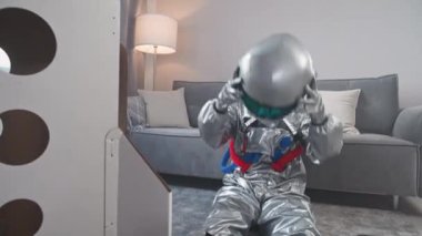Belarus, Minsk - 1 Haziran 2021: Astronot kıyafetli bir adam oturma odasında bir uzay mekiğinin karton modelinin yanında oturuyor, bir astronot miğferi takıyor ve mekiğe bakıyor,.