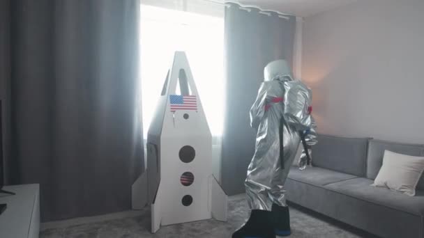 父と息子は自宅のリビングルームで遊びます 宇宙飛行士の衣装の父親 ボール紙のスペースシャトルで遊ぶ少年 家族の日 — ストック動画