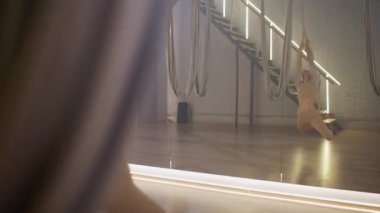 Aynalı odada yoga yapan güzel bir kadın, esnek bir kadın yoga elemanlarıyla güzel bir dans eder, kumaş iplerle odada dans eder..