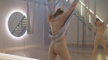 Ayna odasında yoga yapan sportif bir kadın, esnek bir kadın yoga elemanlarıyla güzel bir dans eder, kumaş iplerle odada dans eder..
