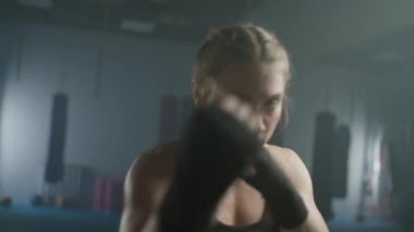 Kadın gücü, genç kadın boksör yumruklarını eğitiyor, boks salonunda antrenman yapıyor, kadın yumrukları seri olarak eğitiyor..