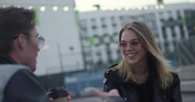 Gençler iletişim kuruyor, kız ve erkek şehir merkezinde modern bir yerleşim bölgesinde konuşuyor, arka planda bulanık ışıklar var..